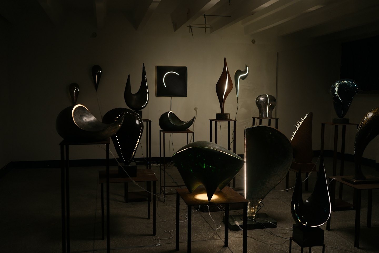 Sculture astratte illuminate su piedistalli in una galleria.