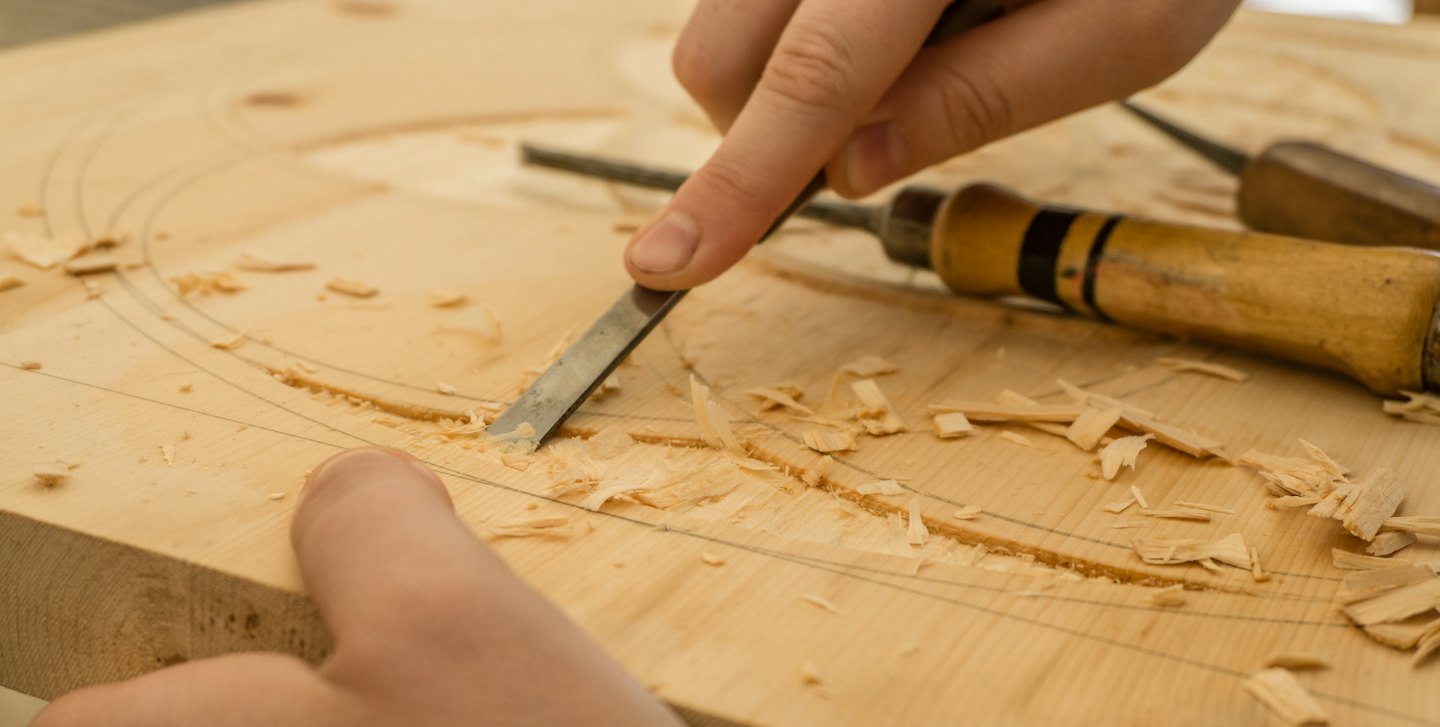 Mani che usano uno scalpello per intagliare il legno.